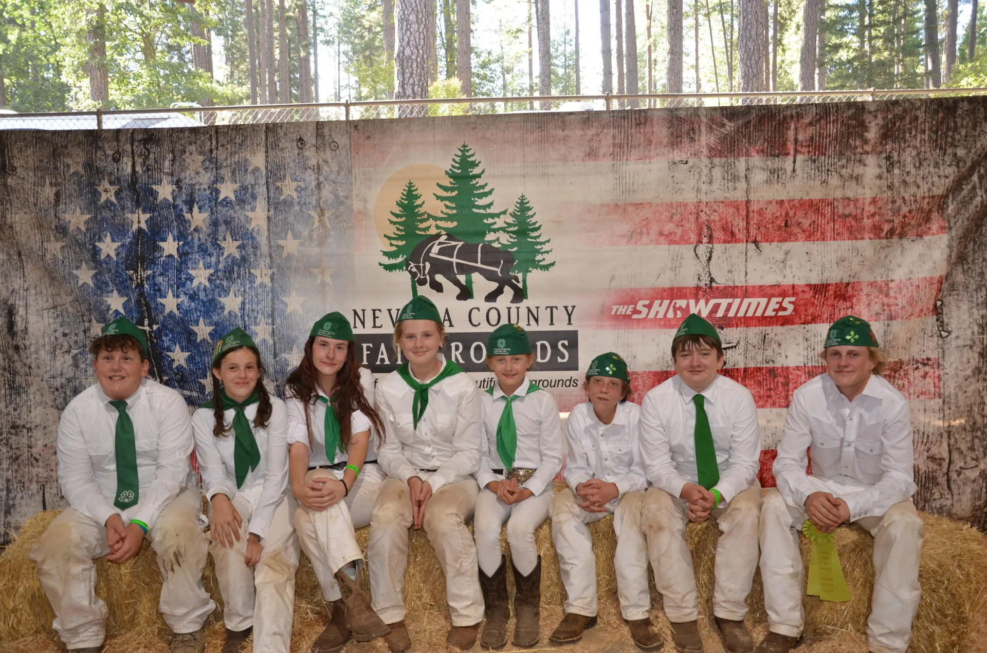 Nevada County 4-H youth wearing their fair uniforms and sitting on straw bales at the Fair.