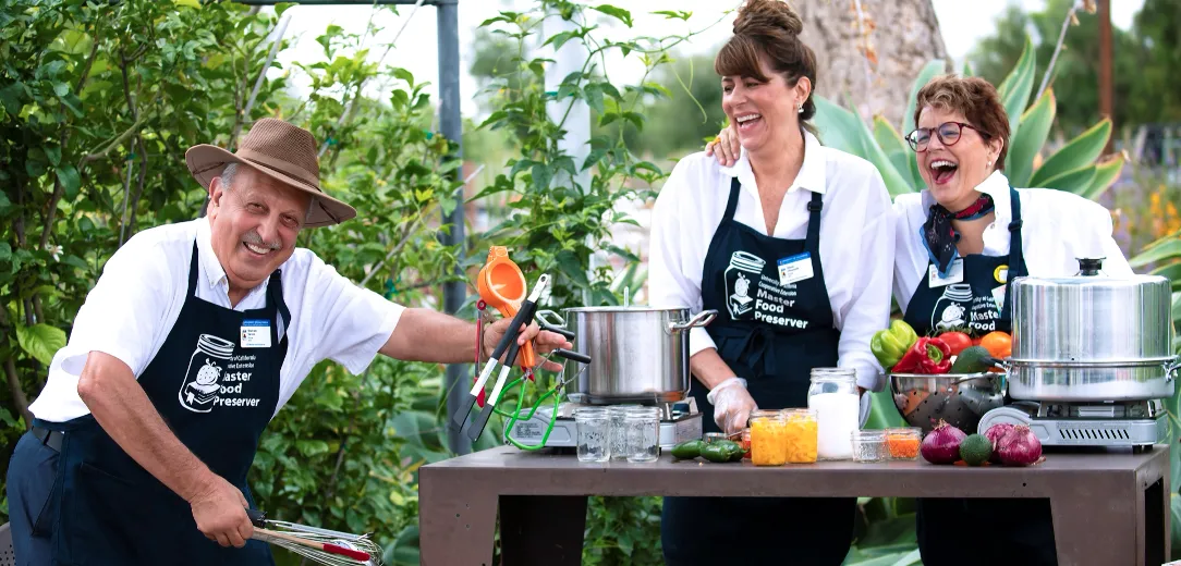 Three Master Food Preservers laughing and posing with a bowl of bell peppers and canning equipment