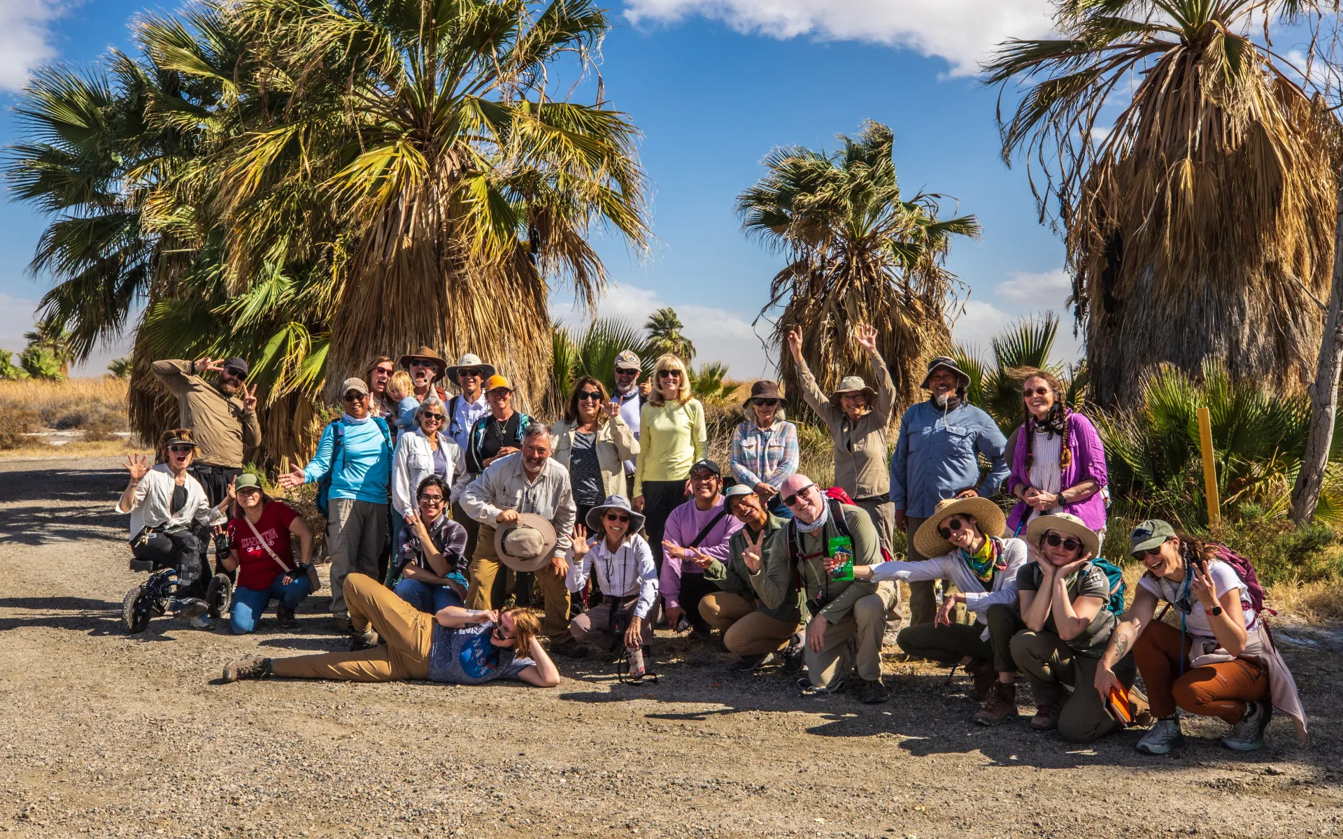 A group of diverse participants smiling and posing in front of palm trees in the deset