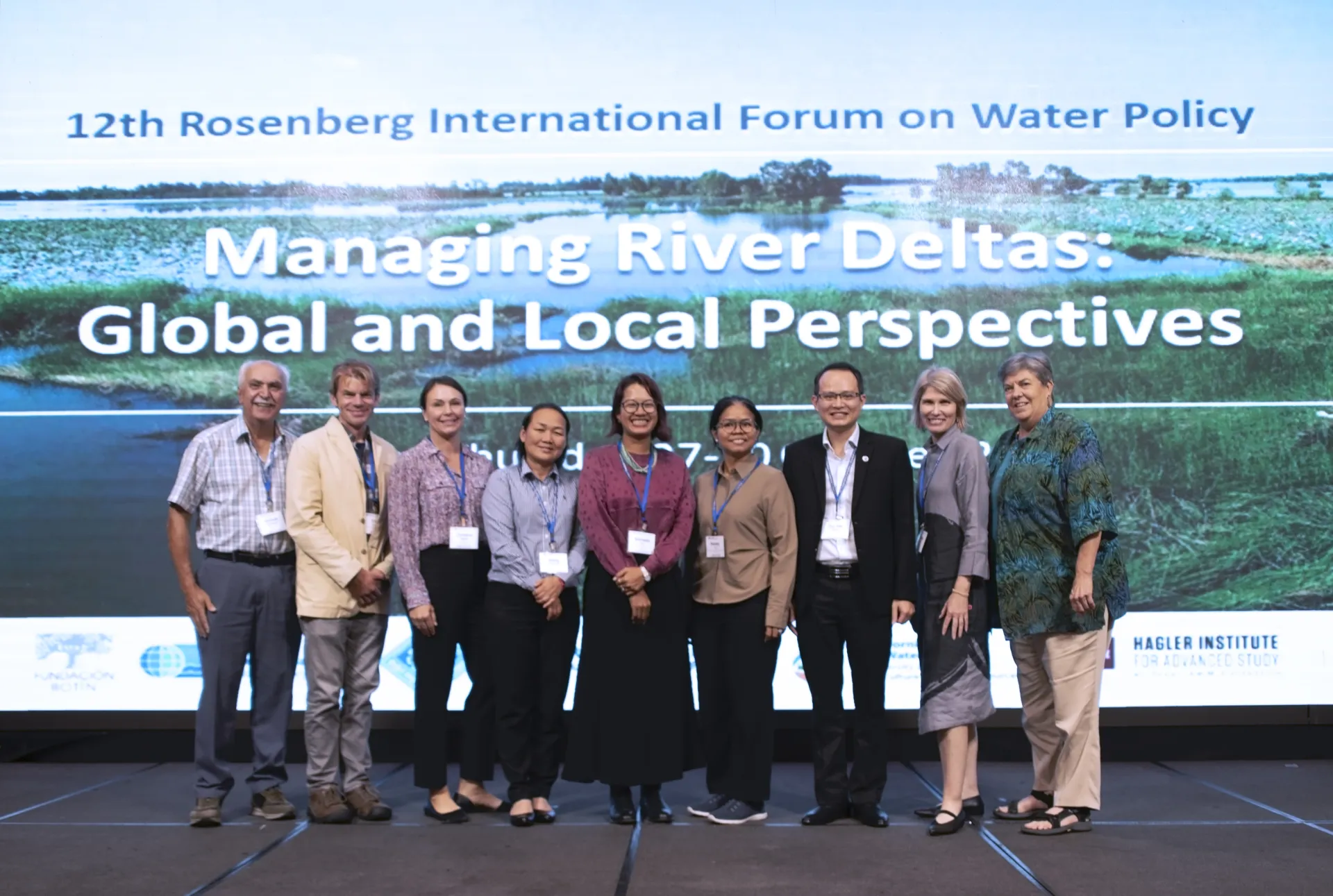 Nine people stand in front of PowerPoint slide that reads: 12th Rosenberg International Forum on Water Policy. Managing River Deltas: Global and Local Perspectives