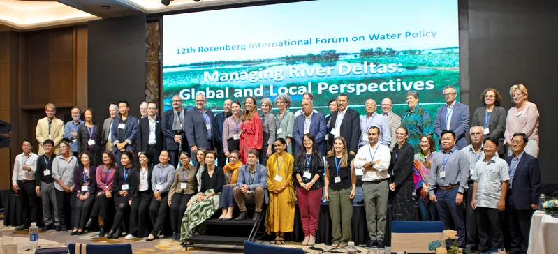 About 50 people stand on stage in front of PowerPoint slide that reads: 12th Rosenberg International Forum on Water Policy. Managing River Deltas: Global and Local Perspectives