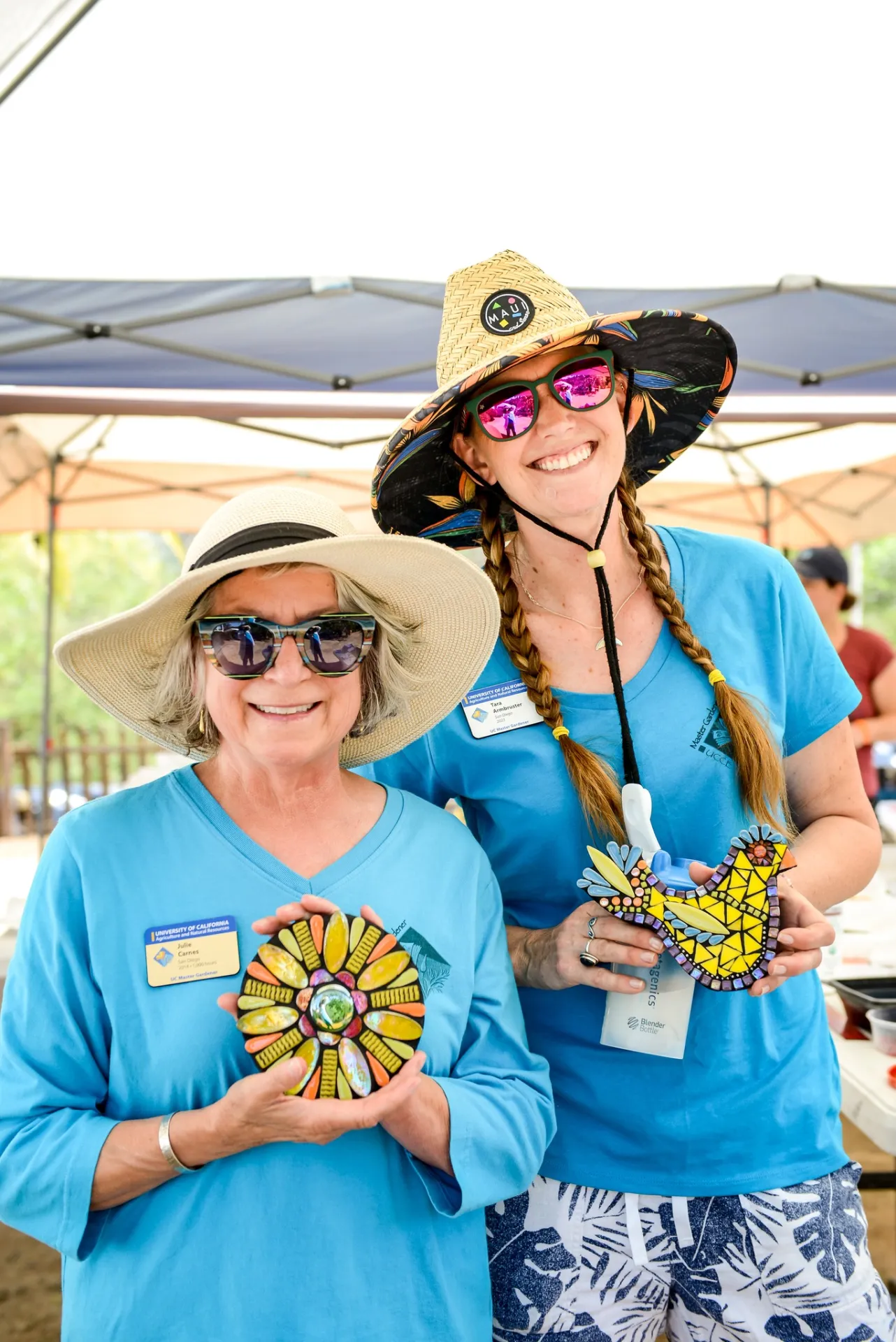 Two smiling women holding mosaic garden art