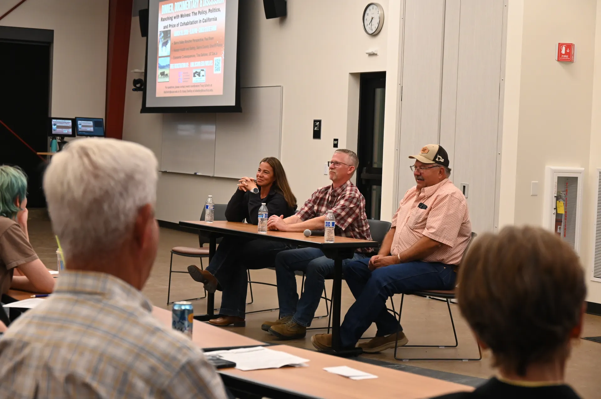 A woman and two men sit at a table facing an audience