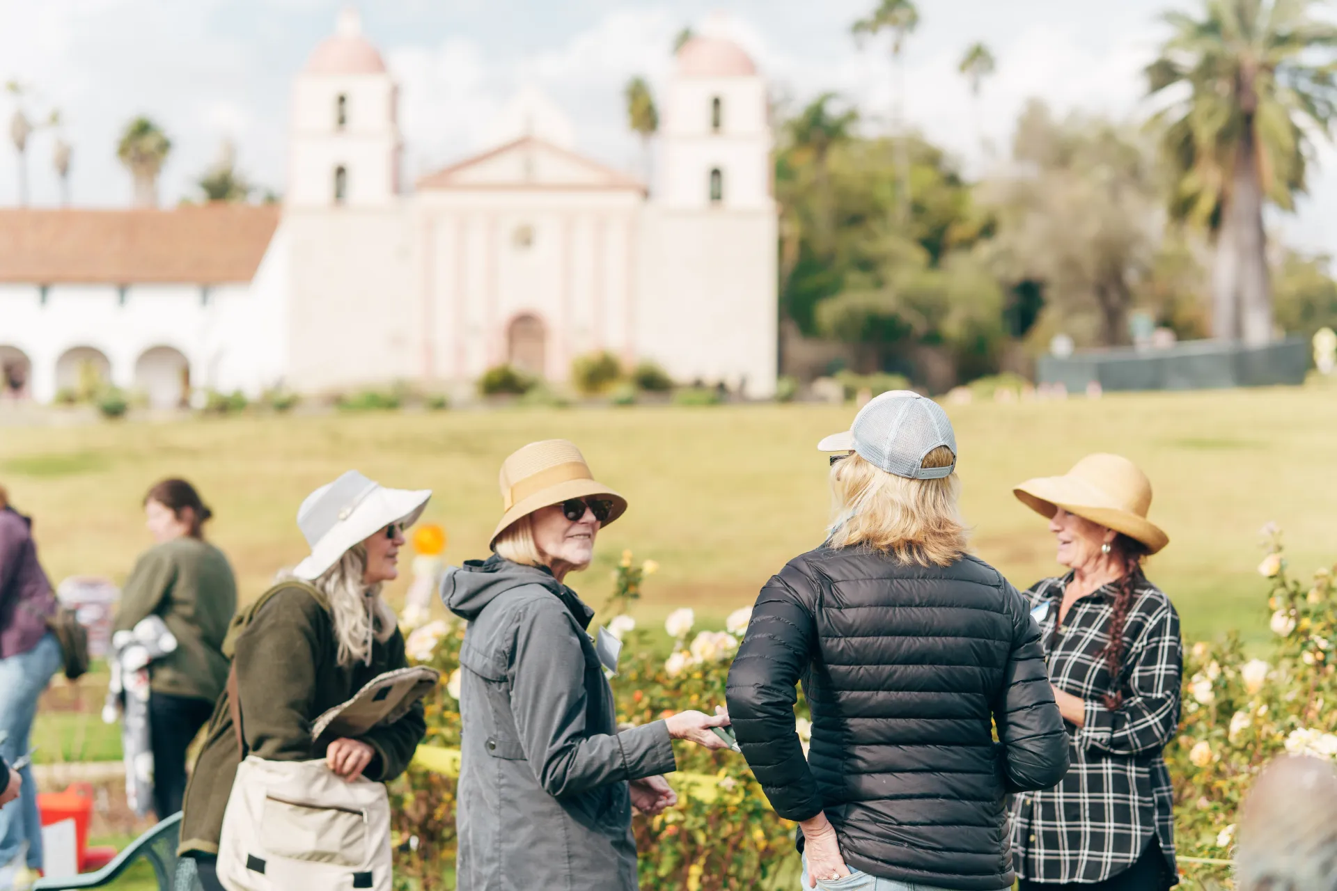Group of master gardeners chatting in front of a rose garden with the Santa Barbara Mission in the background 