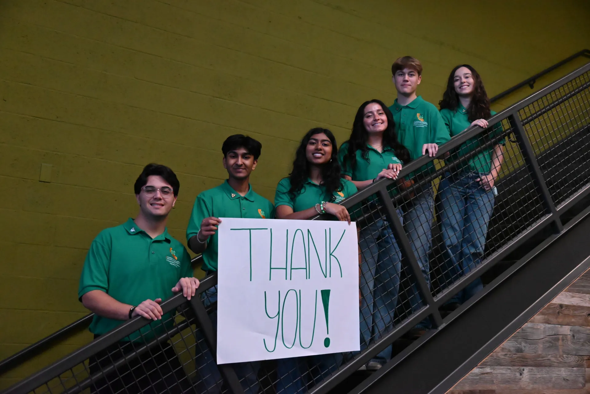 2025-26 State Ambassadors hold a large Thank You sign while standing on the stairs inside ANR building.