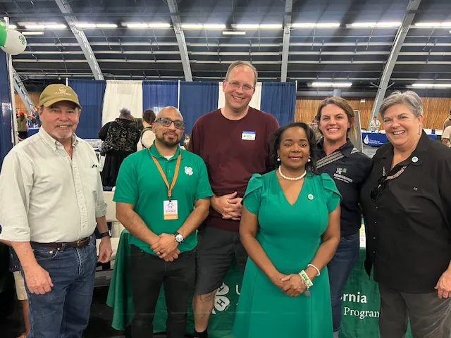 Six people stand in a row. A man and a woman are wearing 4-H green