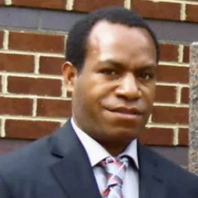 Close-up portrait of Philip Waisen smiling, wearing a navy blazer and tie, standing outside against a brick wall
