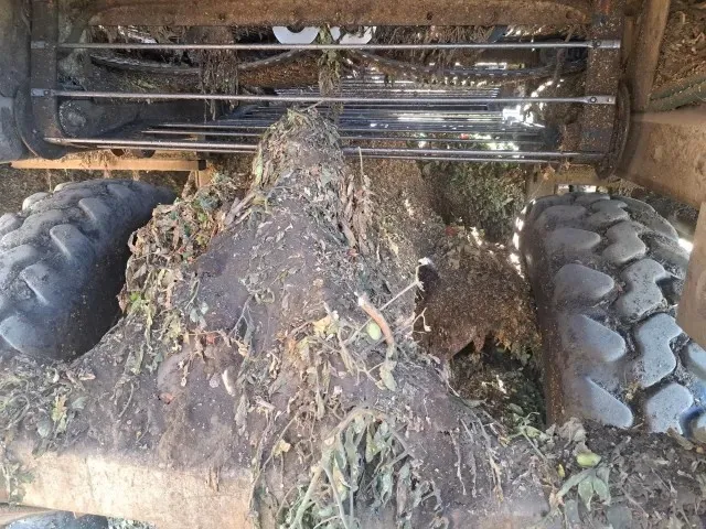 La foto muestra la parte inferior de una cosechadora cubierta de lodo y material vegetal.