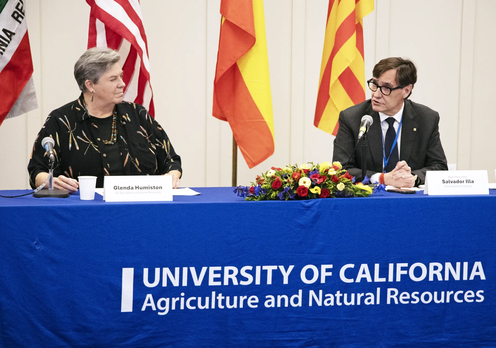 Catalonian President Salvador Illa, at right, speaks into a microphone at a table while UC ANR Vice President Glenda Humiston looks on