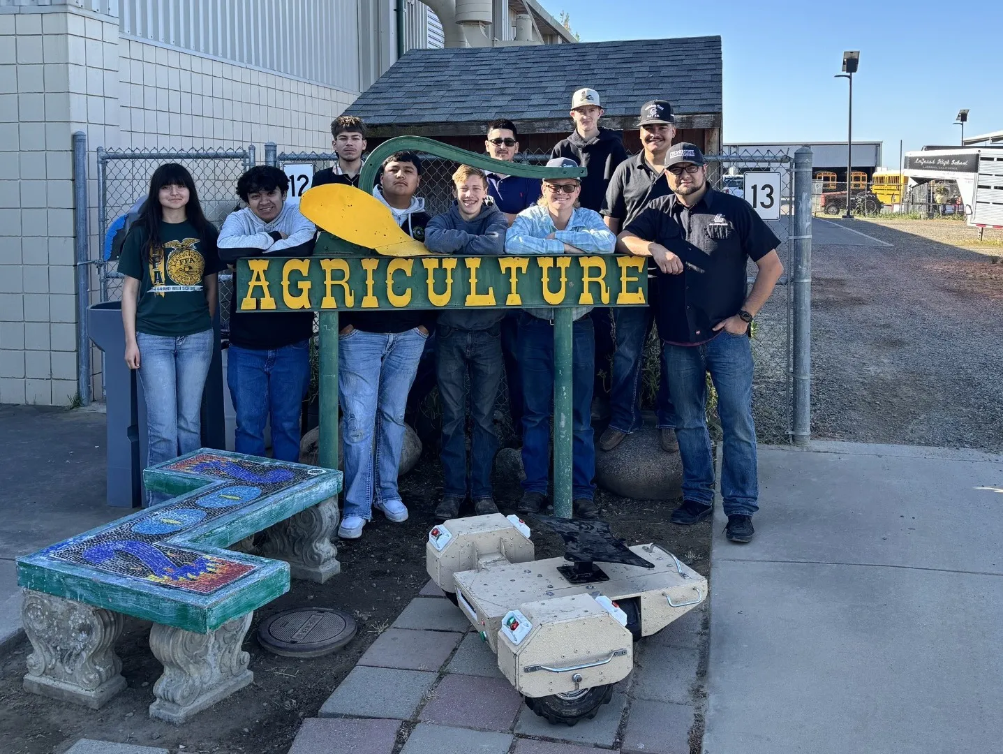 A group of high school students pose by their ag robot and a sign that reads AGRICULTURE