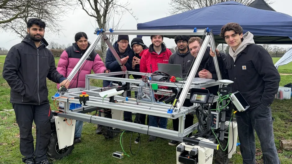 A team of University of Warwick students huddle around their ag robot and pose on a field