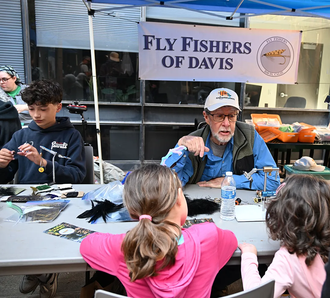 Two fly fishers showing youngsters how to tie a fly.