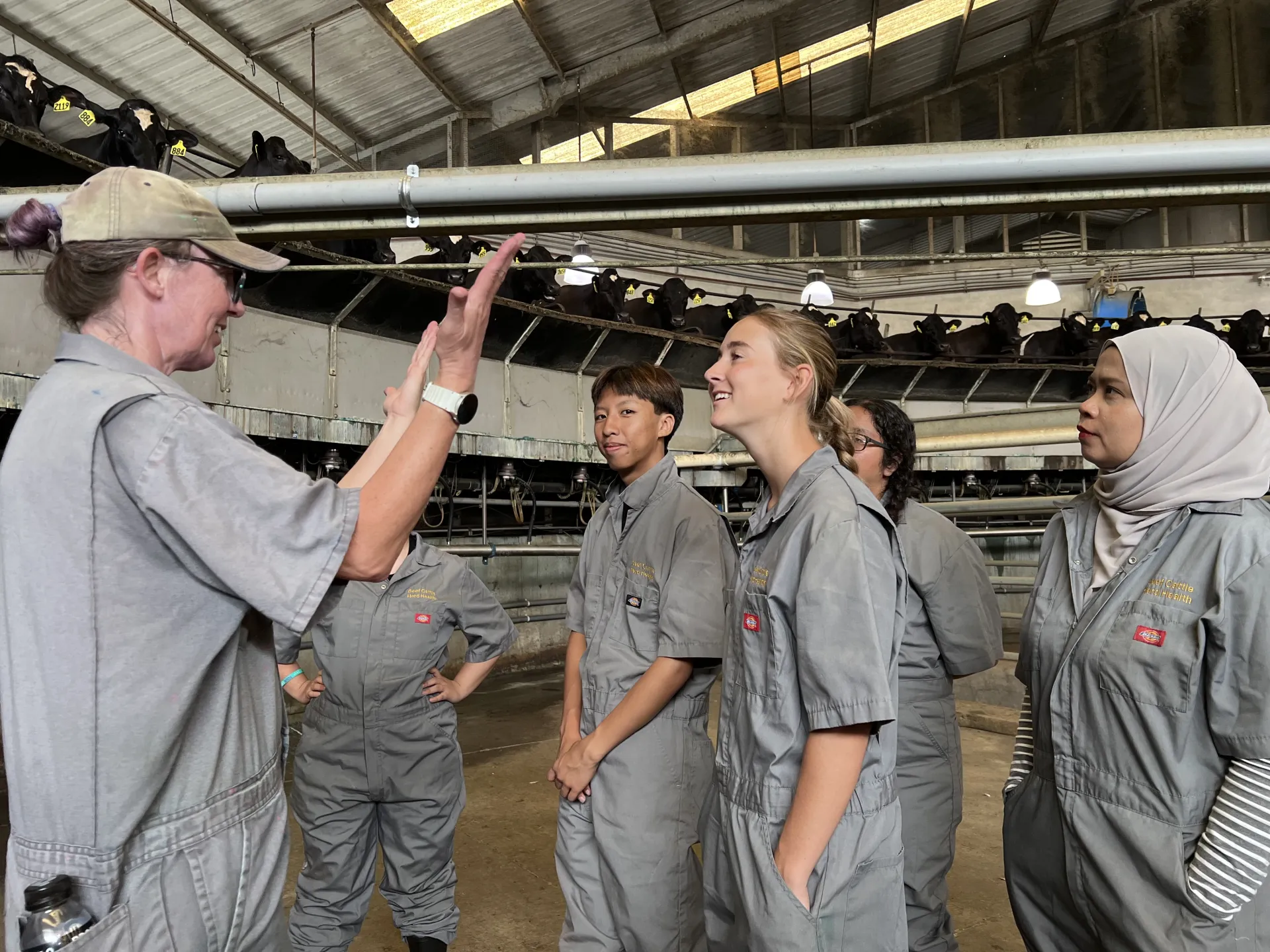 Deniece Williams, left, talks to vet med interns about rotary milking parlors while the cows in the background look on