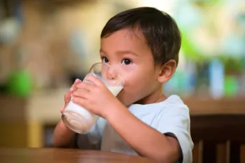 Small child with dark hair drinking glass of milk