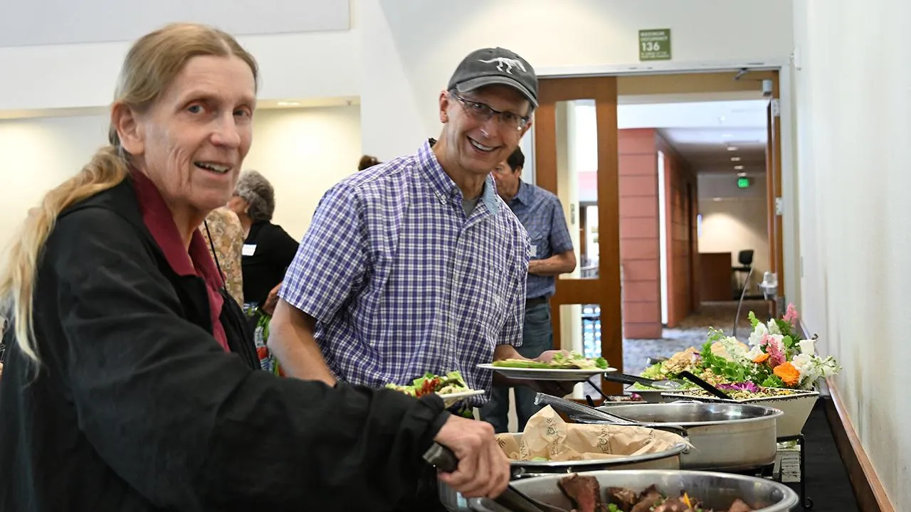 A woman and a man dish up their plates at a buffet table