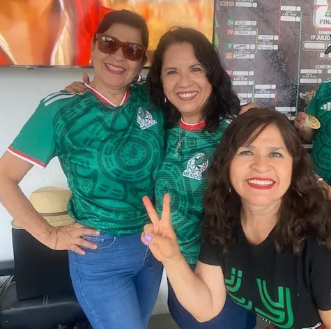 3 friends are watching a soccer game and wearing a Mexico soccer jersey.