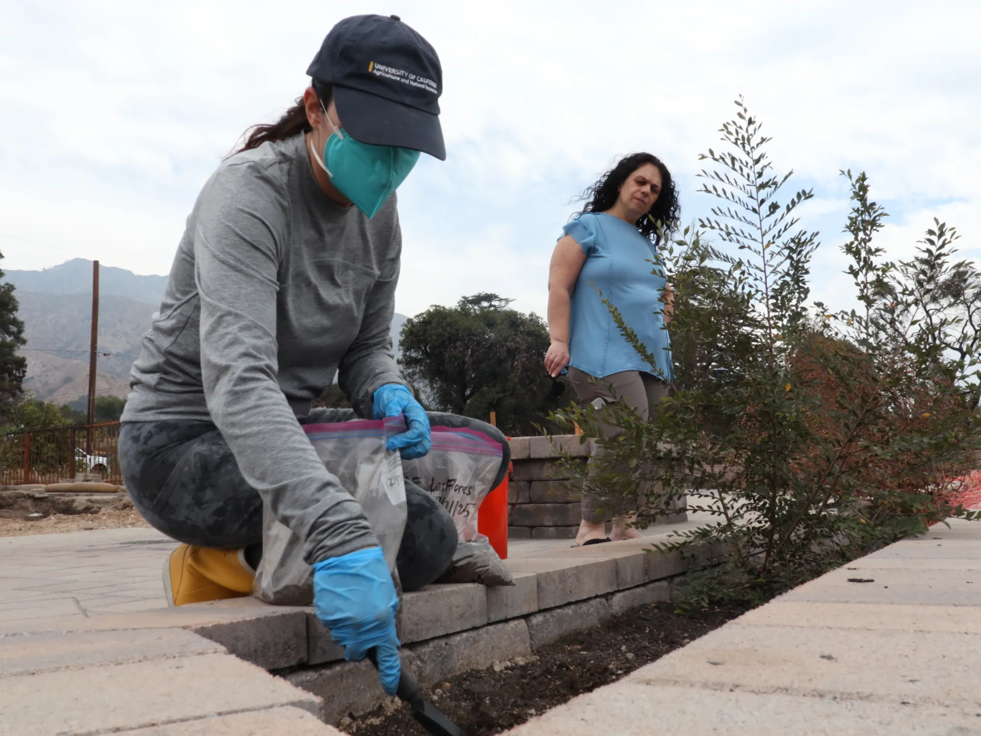 A woman collects a soil sample while another person watches behind her