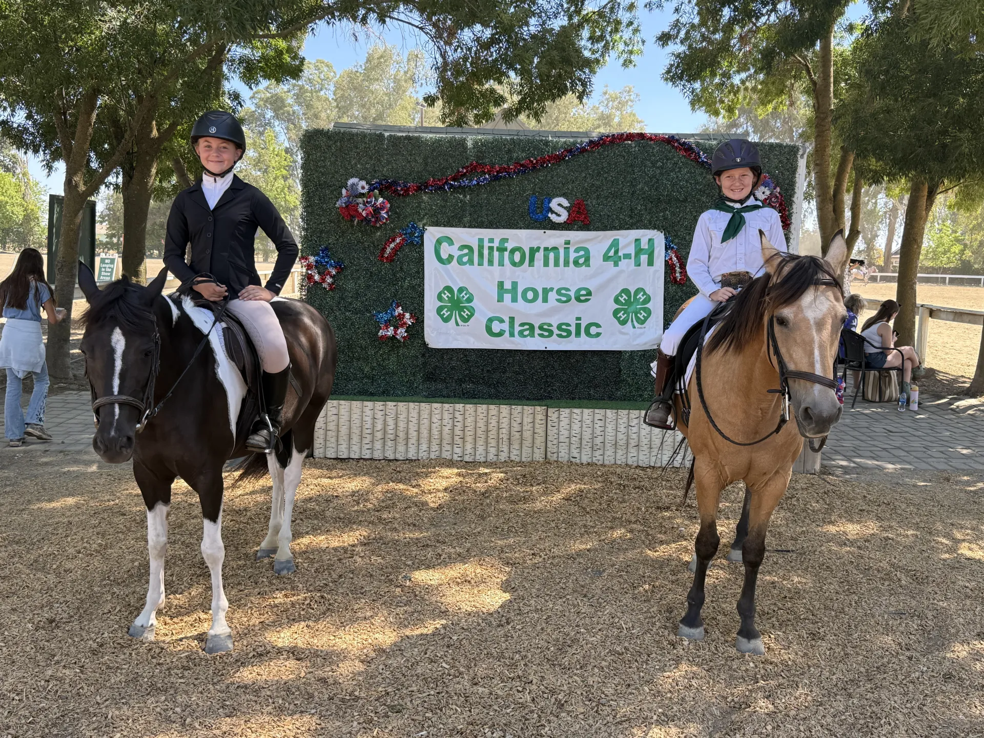 2 youth in English gear on horses in front of California 4-H Horse Classic sign