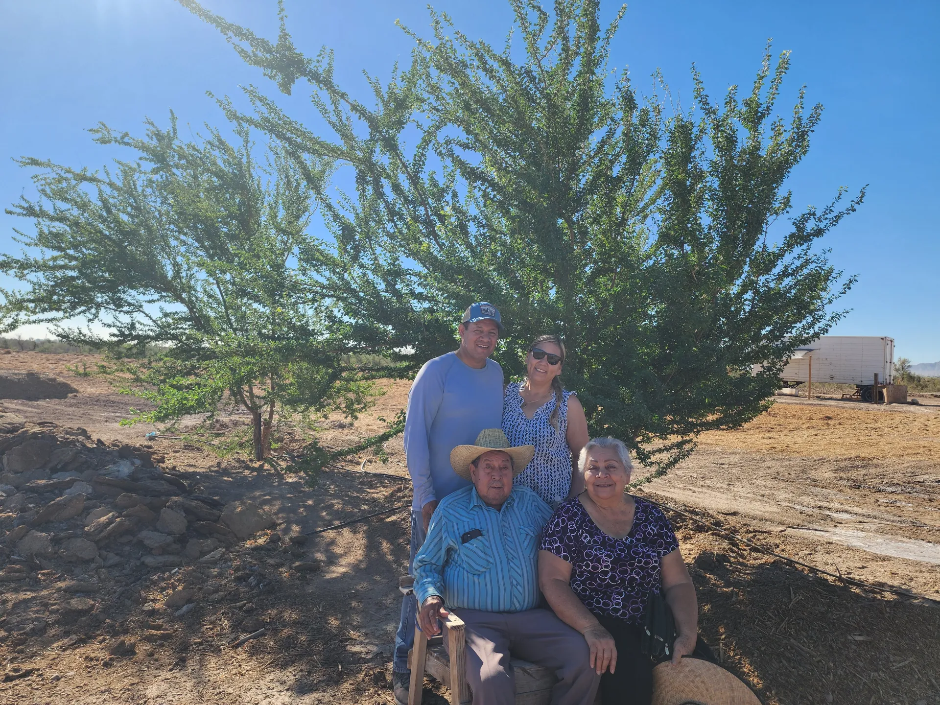 Picture of Israel and Mary, along with Israel's parents, enjoying the shade of one of their young Guamúchil trees at their Rancho La Paz.