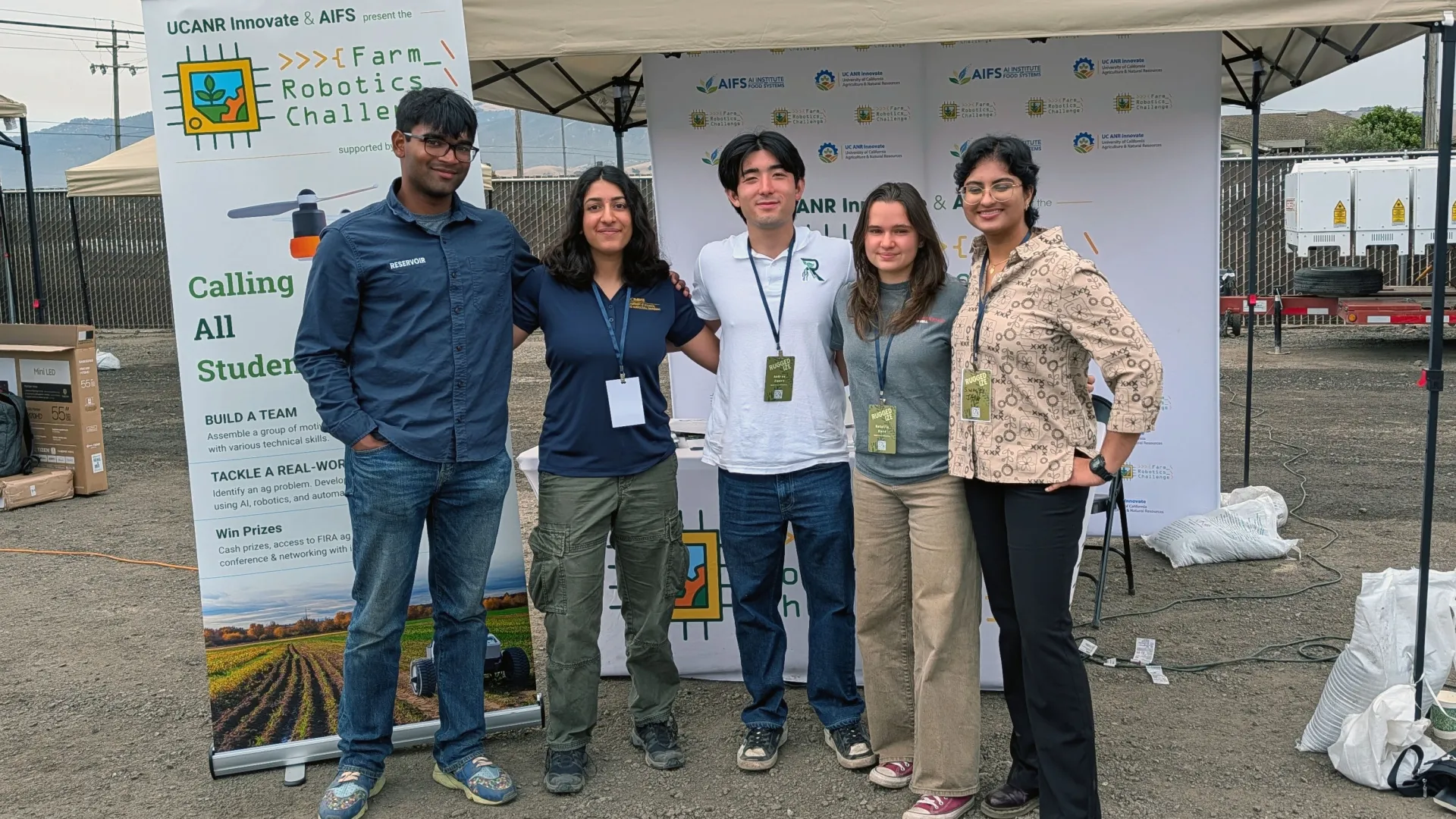 Farm Robotics Challenge alumni stand together in front of an FRC booth