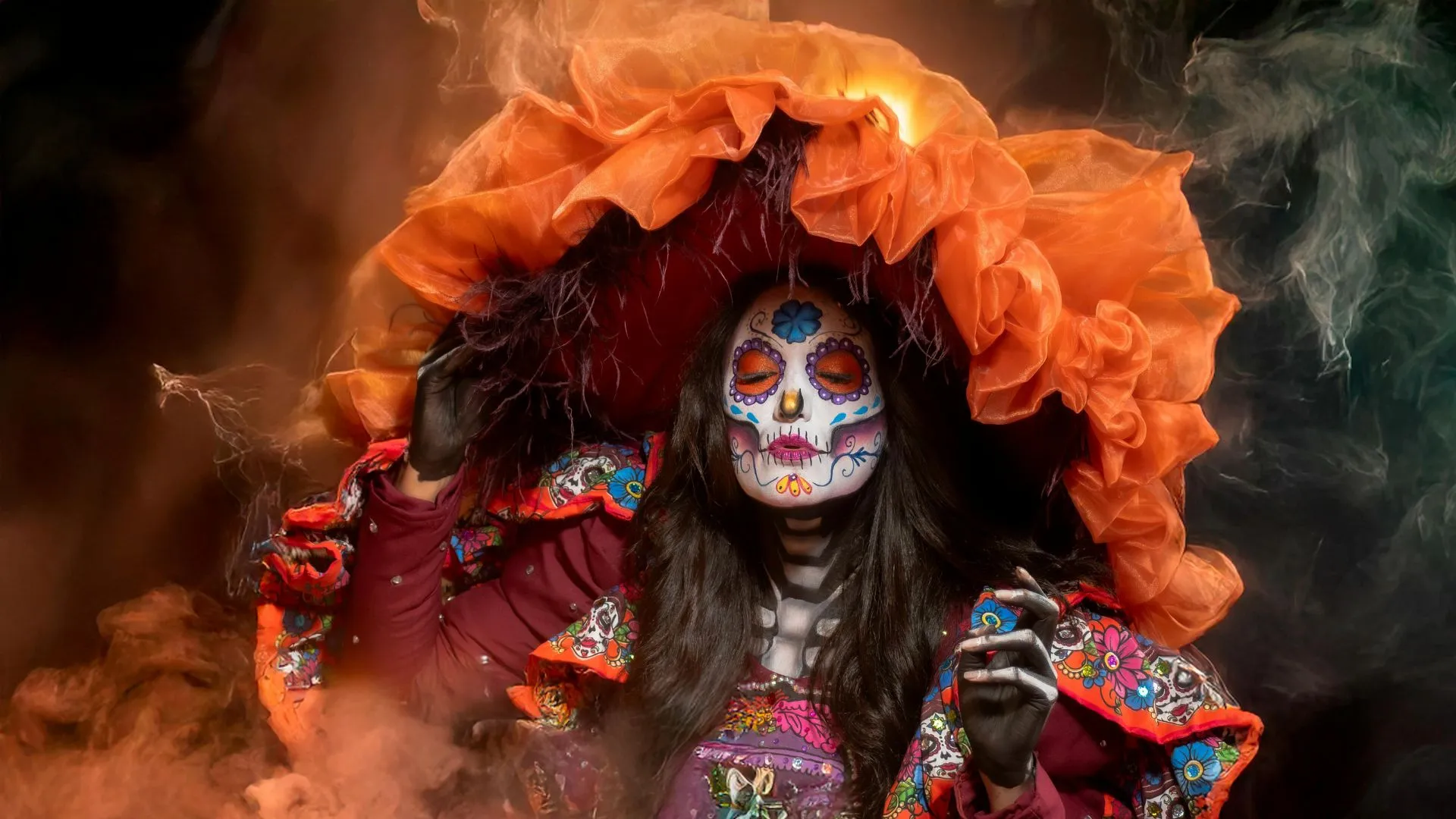 Picture of a Catrina with traditional face paint and bright orange ruffle clothing.