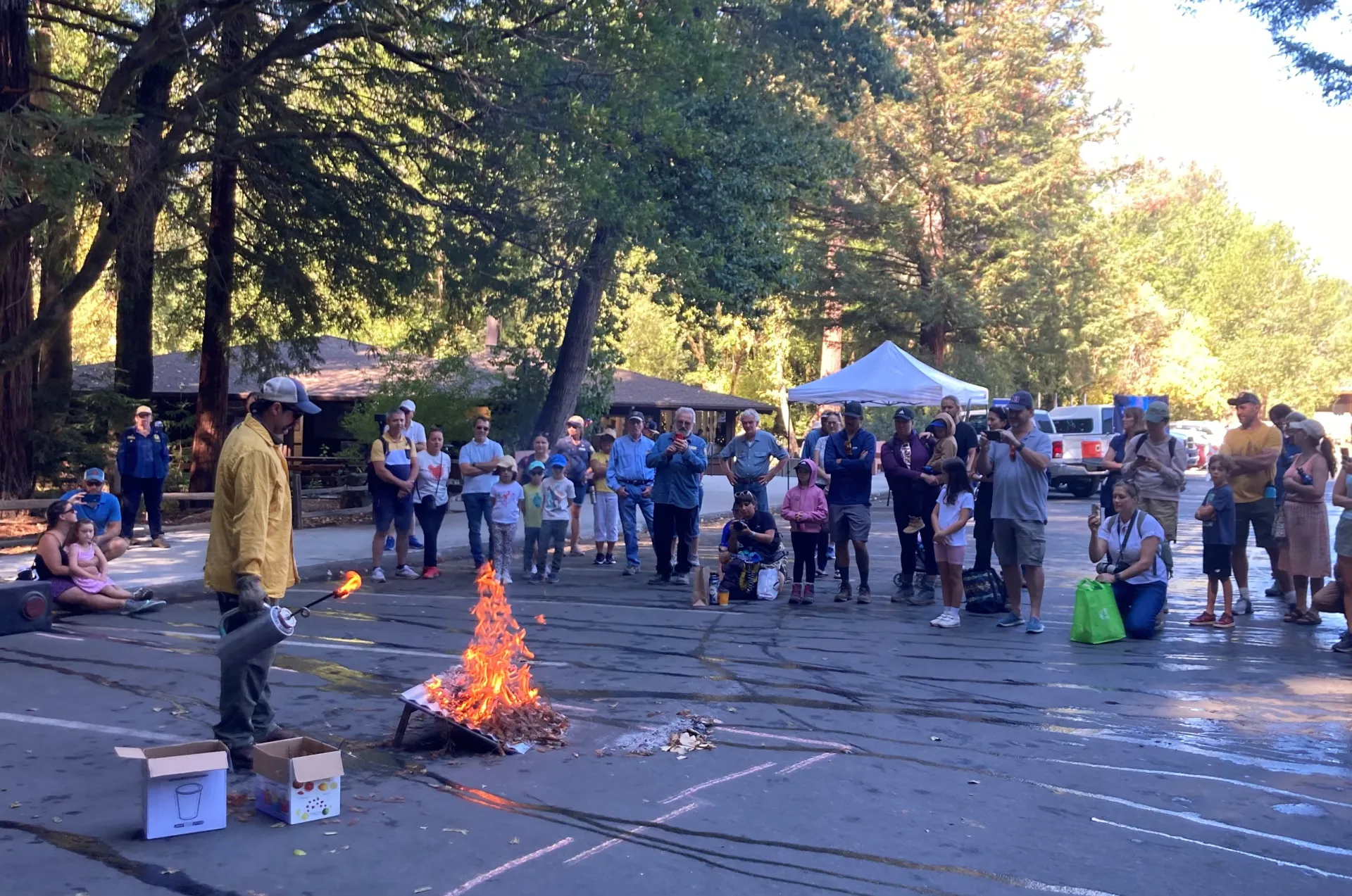 A crowd of kids and adults watch a fire expert light a fire on an inclined board 