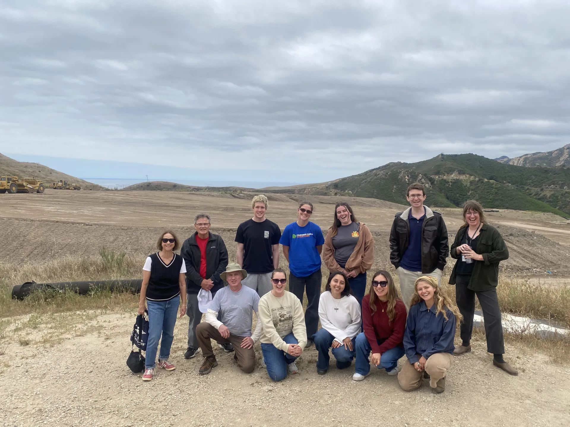 Jason Scott-Sheets, at back in blue polo and dark jacket, smiles during a photo with his Climate Stewards cohort on a field trip to a local landfill as part of the course