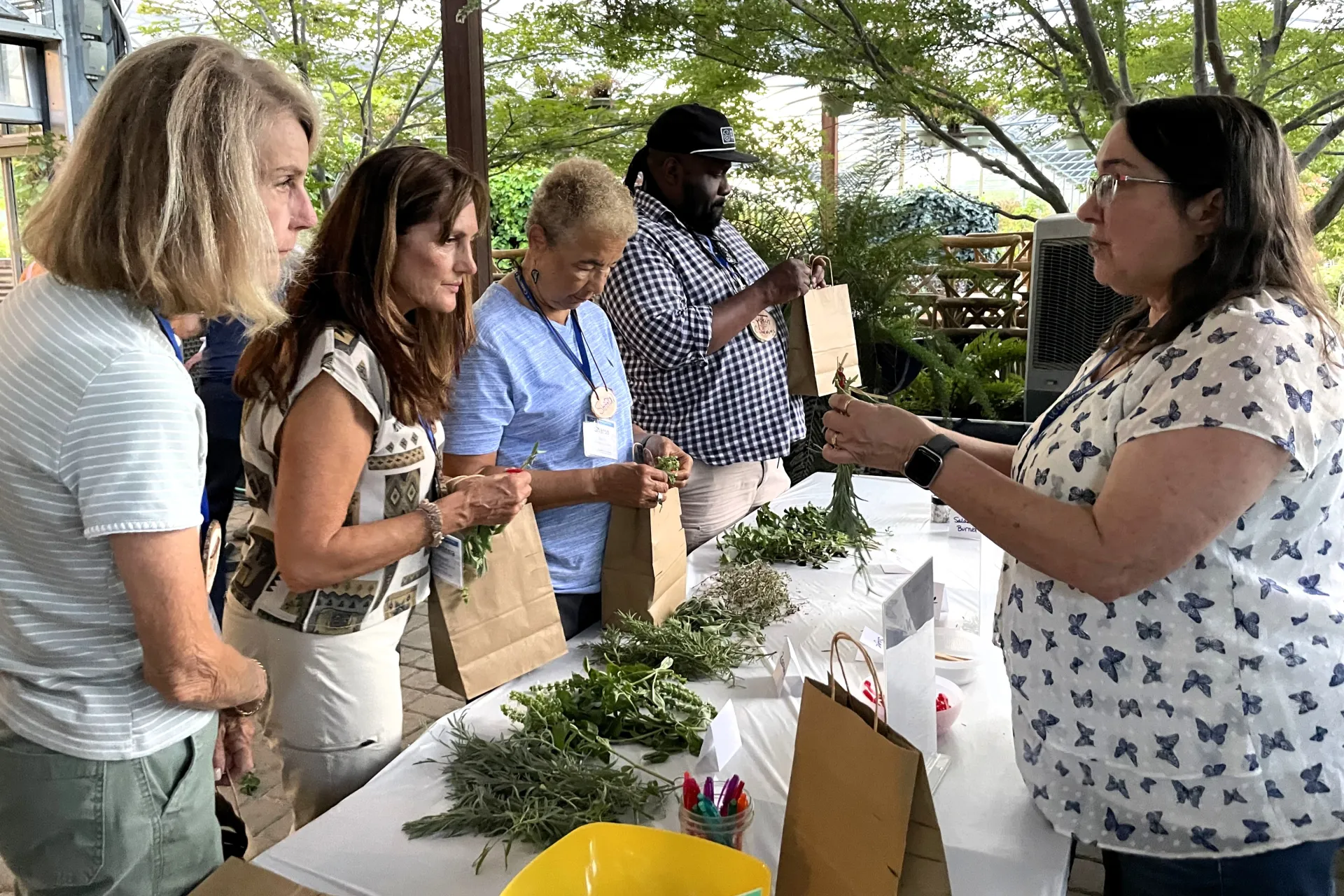 Sue Mosbacher, right, demonstrates how to dry herbs as participants look at array of herbs on a table