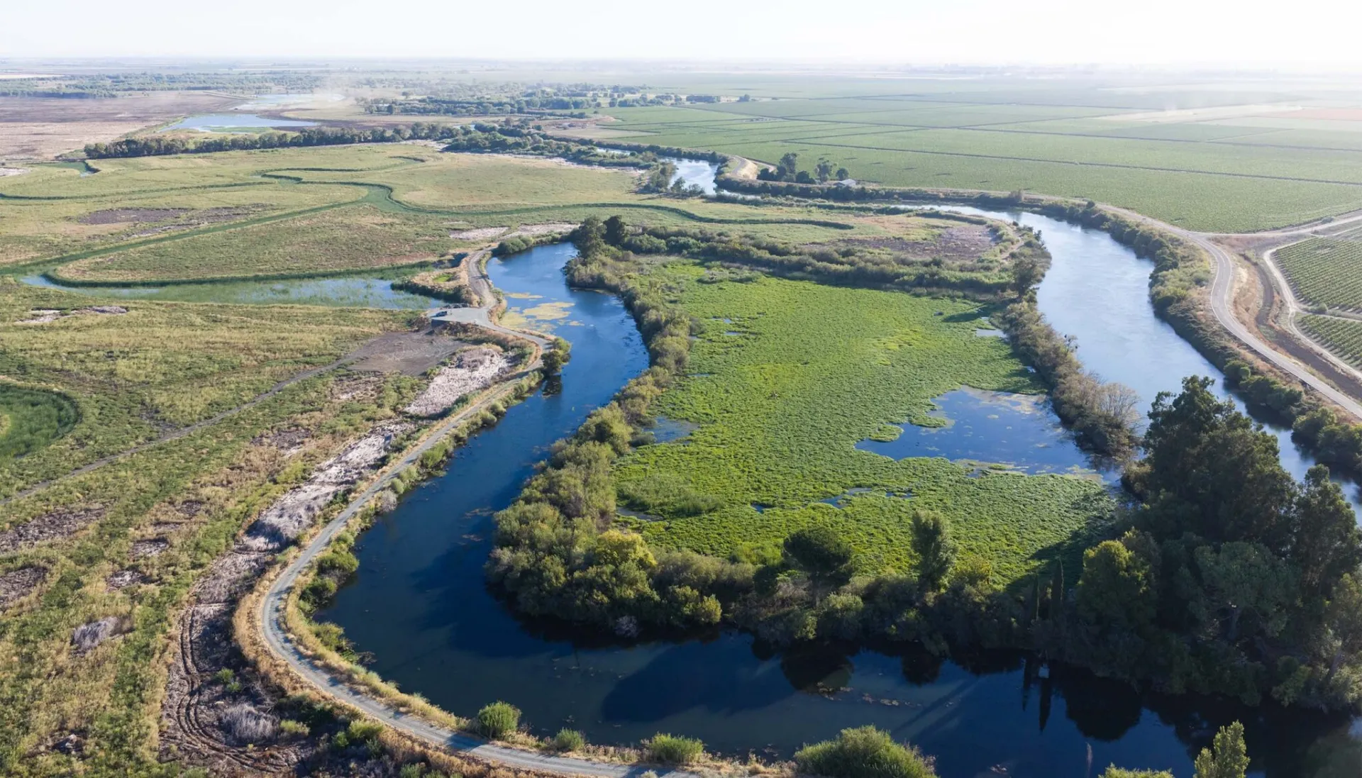 Drone view of a river snaking around land with some shrubs and trees