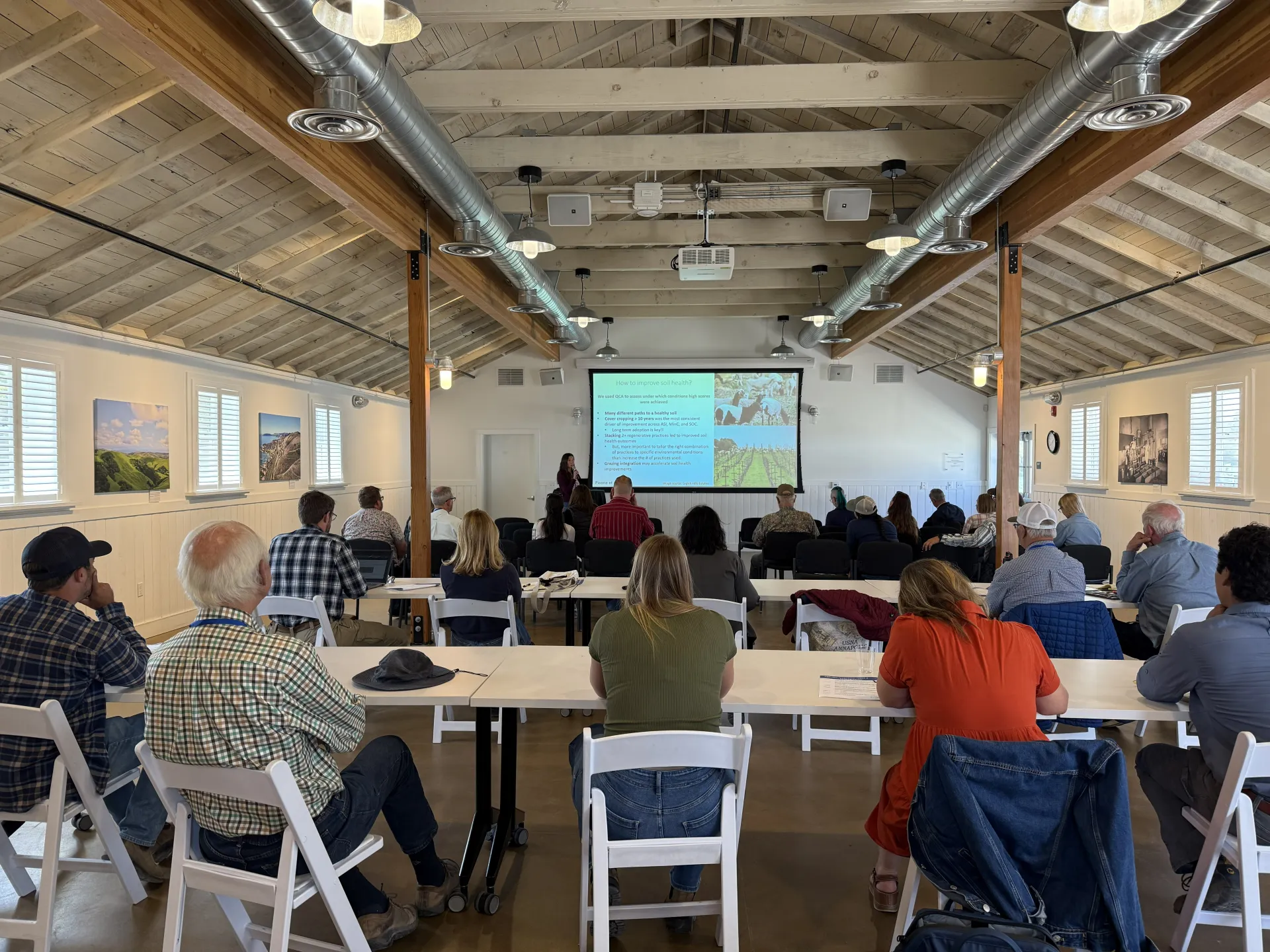 People seated in chairs facing a screen where a presenter is sharing a powerpoint presentation