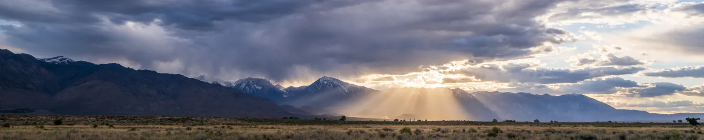 Light rays shining through clouds with mountains in background.