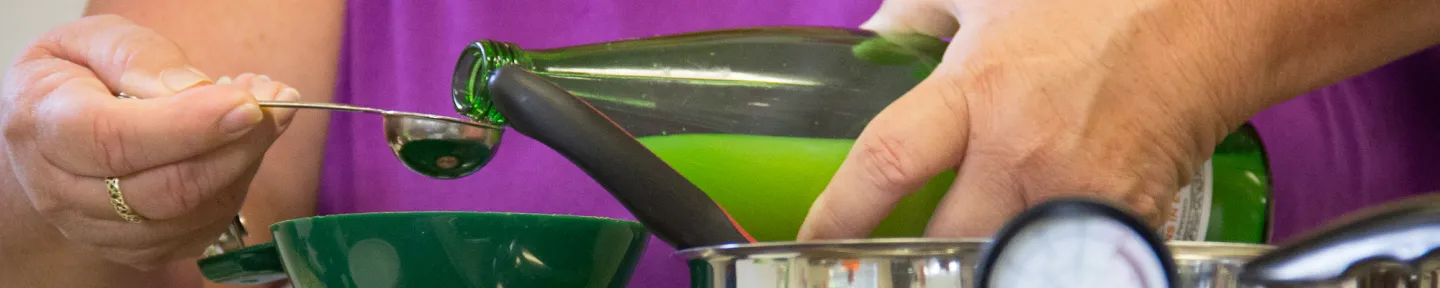 Hands pouring a liquid from a bottle into a small measuring spoon