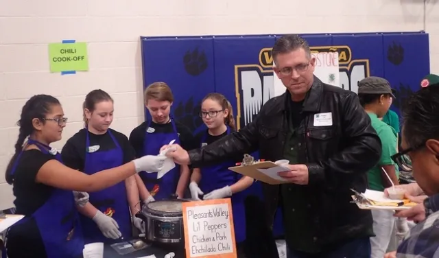 Shawn Windham, agente de la policía de Vacaville y presidente de la Junta de Fideicomisarios del Distrito Escolar Unificado de Vacaville, se prepara para evaluar el chili del equipo Pleasants Valley 4-H, conformado por (de izquierda a derecha) Maliyah Desmarais, Maya Farris, Naomi Lipary y Jessie Means. (Fotografía: Kathy Keatley Garvey)