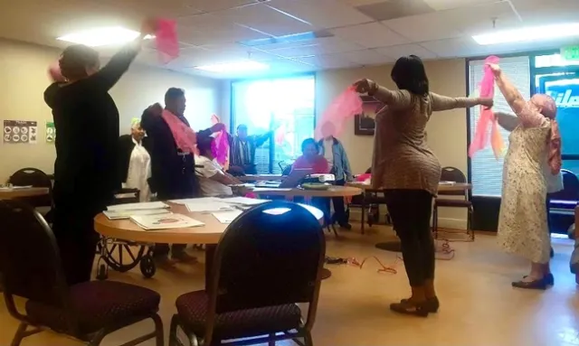 People in a room are standing with their arms extended.