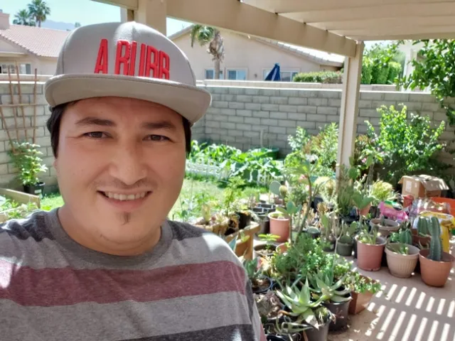Cesar Lopez-Barreras headshot image with dozens of potted plants in the background.