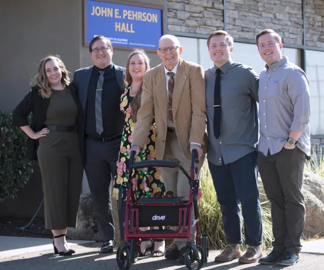 Pehrson smiles as stands surrounded by two granddaughters and three grandsons beneath the building sign bearing his name.