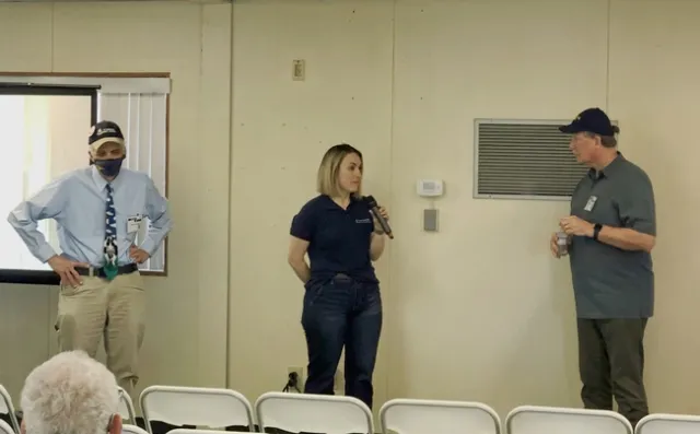 The three academics stand in front of an audience. Jennifer Heguy speaks into a handheld microphone.