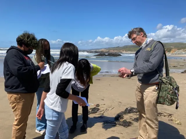 Igor Lacan, asesor de la extensi&oacute;n cooperativa de la UC, a la derecha, describe a los estudiantes de sexto grado algunas de las plantas y animales que viven en el agua de la playa.