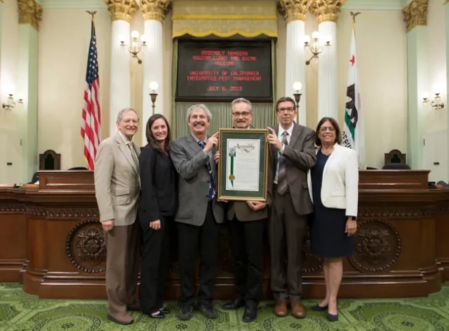 Group stands around Jim Farrar, who holds up a frame proclamation from the Legislature.