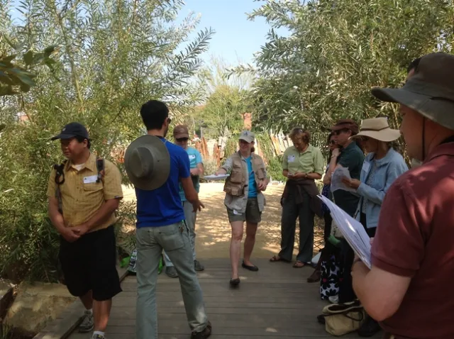 Drill, standing with a group on a foot bridge, hands out papers.