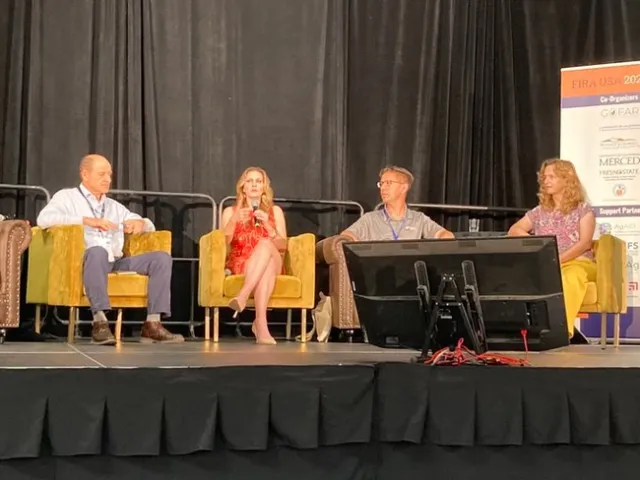 Four people in armchairs. Aubrey Bettencourt, wearing red dress and seated second from left, speaks into mic.