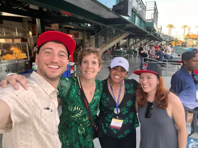 Four people ham it up for a selfie in the stands of the baseball park.