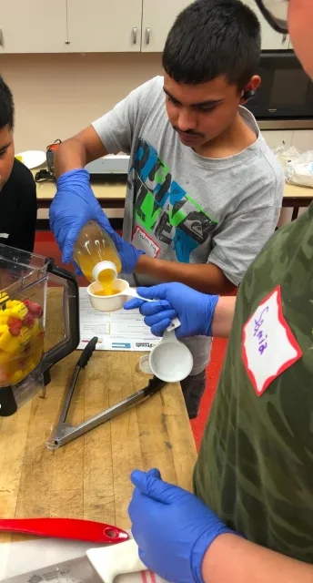 Un estudiante de Teens Love Cooking (Los adolescentes aman cocinar) miden ingredientes para hacer un batido.