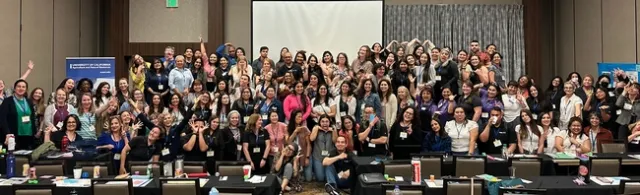 About 100 members of the Community Nutrition and Health network ham it up for a group photo in a conference room.