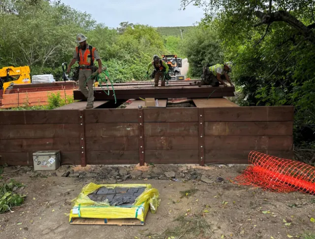 Men wearing hardhats lay down planks for the bridge.