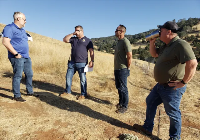 Four men stand in a dry pasture