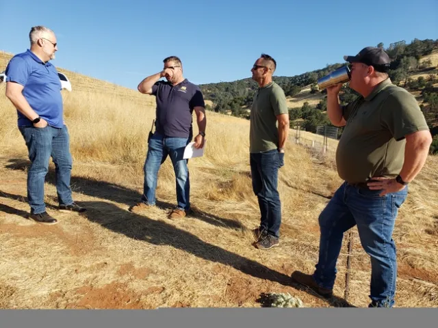 Four men standing on a hillside surrounded by dry grass.