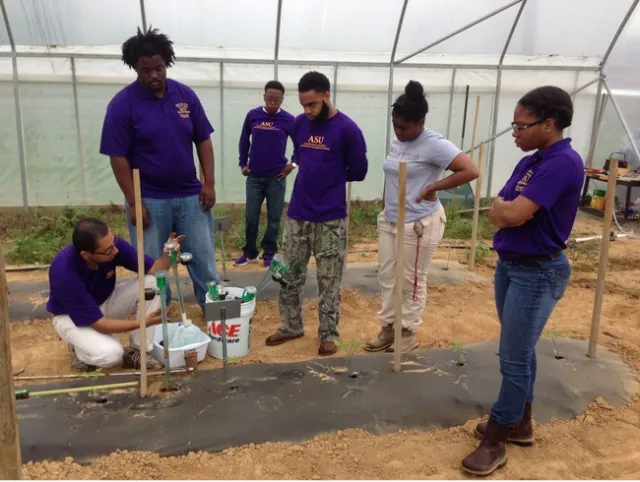A teacher shows students how to use irrigation tools while in the field.