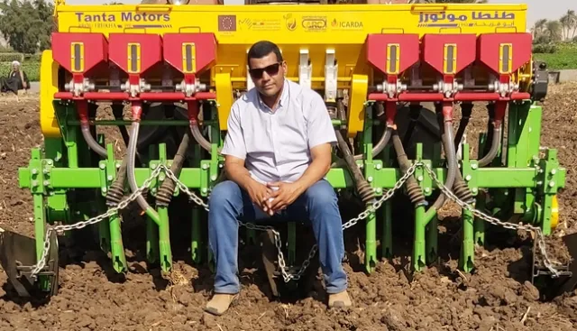 Atef Swelam sits in front of a colorful piece of farm machinery