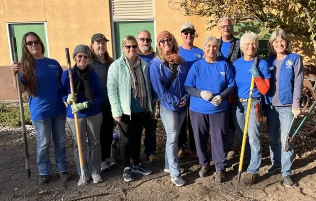 Smiling group of people, standing in two rows while holding gardening tools.
